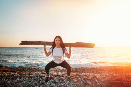 Concept of sport and healthy lifestyle. A woman in sportswear raises a log, engaged in strength...