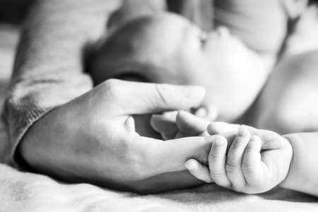 The baby is holding on to the mother's finger. Hands close-up. Black and white photo. Side view. Concept of motherhood and children's day.の写真素材