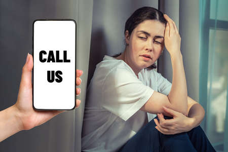 Portrait of stressed woman clutching her head with her hand. Hand with a smartphone with a call the...