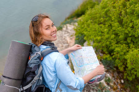 A pretty tourist woman sits on a stone mountain path with a map in her hands. Hiking and sports....