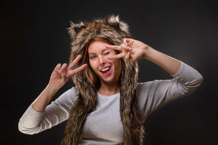 Concept of christmas holidays. A young beautiful woman in a fur hat with ears, and woolly mittens, smiles provocatively, narrowing her eyes. Black background. Copy space.の写真素材