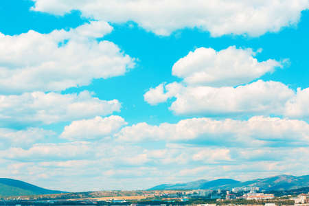 Landscape. Blue bright sky with white cumulus clouds over a mountain valley with a settlement.の写真素材