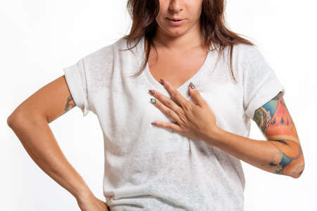 World heart day. A young woman with a tattoo on her arm grabs her chest. White background. Close up....