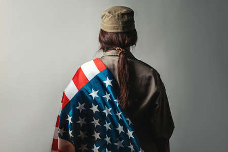 Celebration in the USA. A female soldier holds an American flag on a gray background on her...