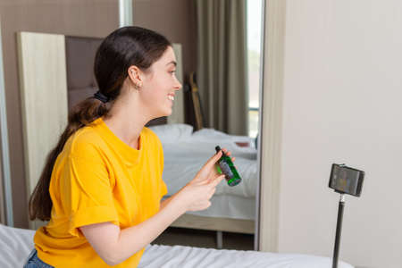 Portrait of young pretty female vlogger streaming live video on smartphone and sshowing a new...