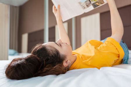 Reading and education. A woman reads a magazine lying on the bed. Indoor. Close-up view from behind the head.の写真素材