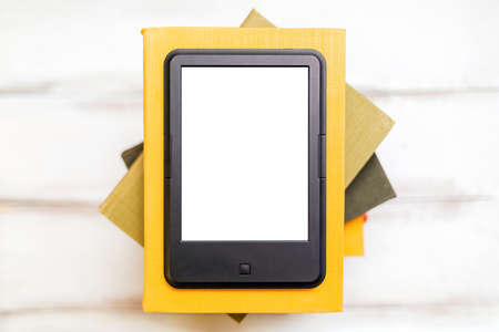 Reading and knowledge. E-book reader is on top of a stack of books on a wooden background. Flat lay. Mock up. Concept of education and electronic gadgets.の写真素材