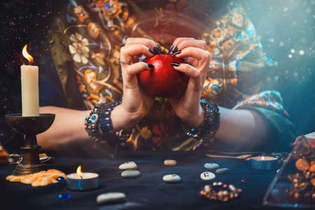Astrology and divination. A fortune teller holds a red apple in her hands. On the table lay runes, candles, talismans. Close-up of hands.の写真素材