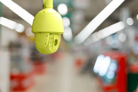 CCTV. Yellow surveillance camera on the background of the blurred trading floor of the store.
