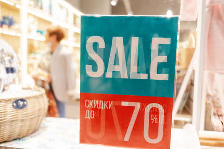 Sale. A sign with a notification about discounts and sales, hanging on a glass shop window. In the background in a blur a person who visited the storeの写真素材
