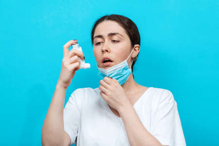 Asthma. Portrait of young woman takes a medical mask to make the inhalation of medication. Light blue background.の写真素材