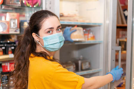 Portrait of a female employee with a medical mask on her face and rubber gloves, opening a...