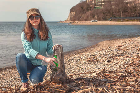 A young woman puts the collected garbage in a bag and posing for the camera. Cleaning of the coastal zone. Tint.の写真素材