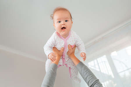 A mother lifted the happy child in her arms. Bottom view. White interior. The concept of motherhood and happy childhood.の写真素材