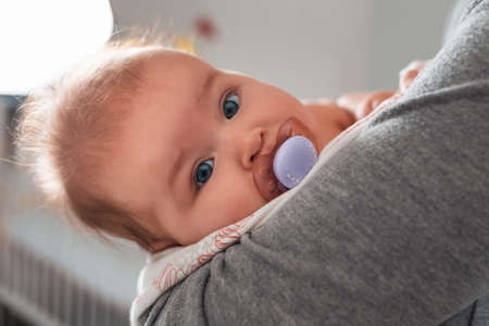 A mother lulls a baby in her arms with a pacifier in her mouth. Close up portrait of a child....