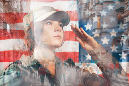 National holidays in the United States. Portrait of a female soldier saluting, against the background of the American flag. Side view. Double exposure.の写真素材