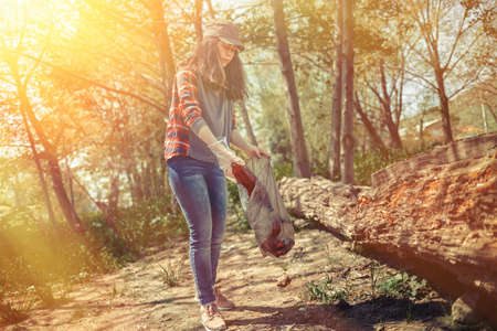 Woman volunteer helps clean the forest of plastic garbage. Earth day and environmental improvement concept. Tint and light.の写真素材