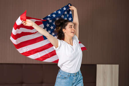 Portrait of a young happy woman waves an American flag. Indoor. The concept of the American national holidays and patriotism.の写真素材