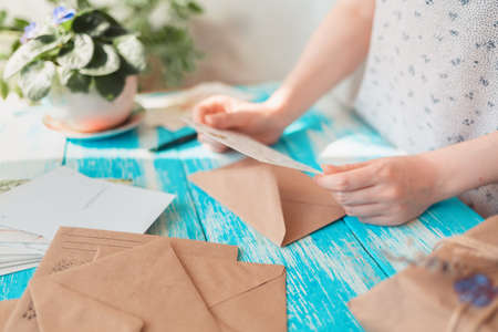 A woman reads a postcard. Hands close-up. Blue wooden table with a parcel in the background. The concept of postcrossing.の写真素材