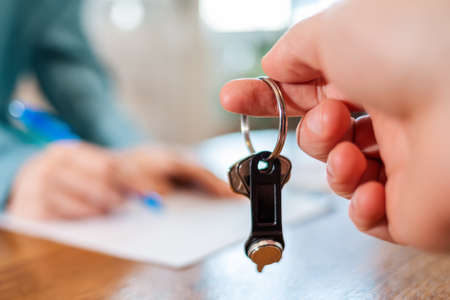 A man's hand holds the keys. In the background, in a blur, a person is signing documents. Hands...