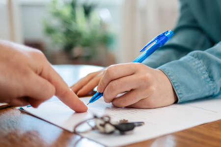 A realtor points to the contract for signing. Hands close-up. There are keys on the table. World...