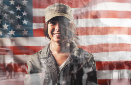 Celebration in the USA. Portrait of a smiling female soldier posing against the background of the American flag. Double exposure.の写真素材