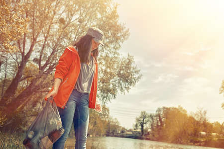 A woman volunteer on a scavenger hunt on the river. Trees and a river in the background. The concept of environmental protection. Tint and light.の写真素材