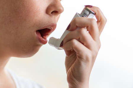 Asthma. The woman brings the inhaler to her mouth. Close-up of the hand and lower half of the face. Blurry backgroundの写真素材