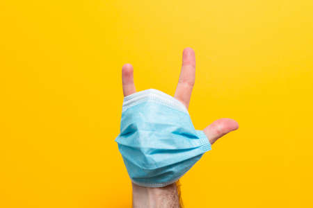 A man's hand with a mask on, fingers spread. Yellow background. The concept of protection from the...