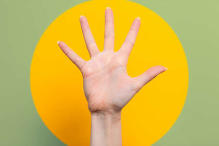 A woman's hand with outstretched fingers. Green background with a yellow circle. Close up. The concept of hypnosis, influence, and psychology.の写真素材