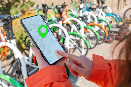 A female's hand holds a smartphone and uses an online map. Bicycle parking is in the background....