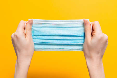 Female's hands hold tight medical mask. Yellow background. Close up. Concept of protection against...