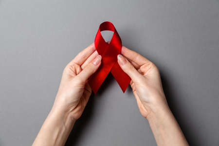 Woman's hands hold a red ribbon, a symbol of the fight against AIDS. Gray background. Copy space. Flat lay. The concept of world AIDS day.の写真素材