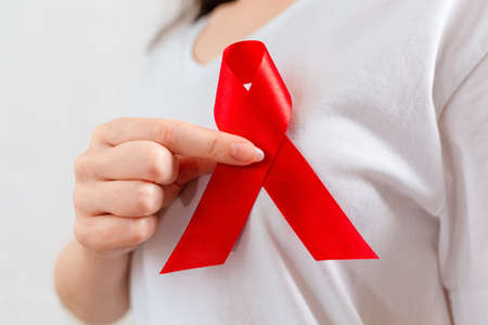 A woman holds a red ribbon on her chest with her fingers. Hands close-up. The concept of world AIDS day.の写真素材