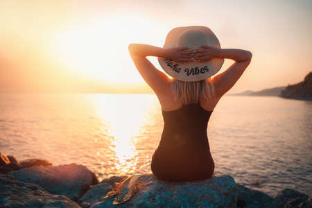 Summer holidays. A woman in a straw hat sits on the beach. Sunset. Rear view.の写真素材