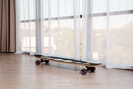 The longboard stands on the floor near a large window in the room. Nobody. Skateboarding and extreme sports.の写真素材