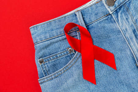 Jeans with a red ribbon. Red background. Flat lay. Close up. Copy space. The concept of the world...