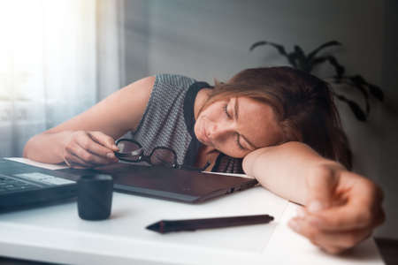 Young woman sleeping in the workplace. Fatigue and overload in office work. Morning light.の写真素材