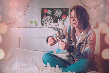 young girl sitting on the bed with a smile makes a snowflake out of paper in a warm tint.
