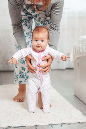 A mother holds the baby in her hands and teaches him to walk. Home interior. Concept of teaching...