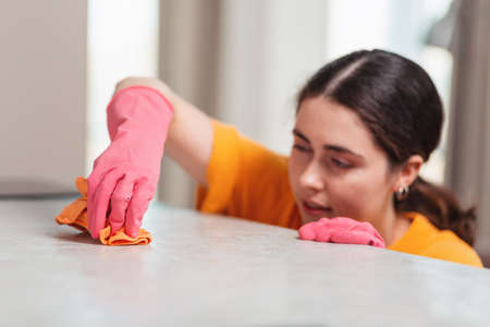 Blurred portrait of a young woman in rubber gloves is busily wiping the table with a rag. Close-up....