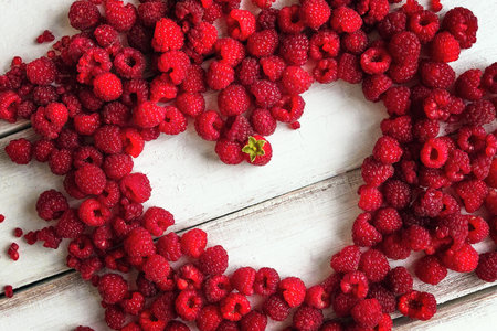 sweet raspberry is laid out in the shape of a heart on a wooden white table top.