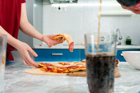 Female hands holding a slice of pizza. A glass with a drink in the foreground. Close up. The concept of junk food.の写真素材