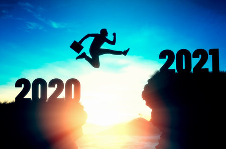 2021, calendar. Silhouette of a businessman jumping over a cliff, from one cliff to another. In the...