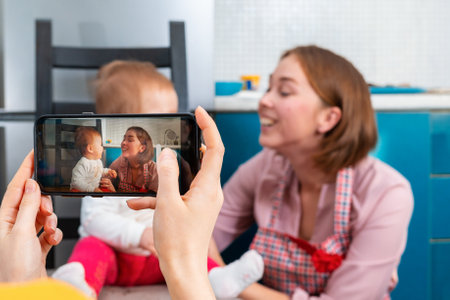 Female's hands shoot a portrait of a mother and child on a smartphone. Family in the background in a blur. The concept of modern technologies in everyday life.の写真素材