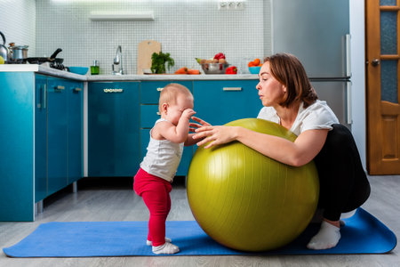 Yoga at home. A young mother leaning on a fit ball, calms her crying baby. The concept of fitness with children at home.の写真素材