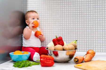 A little kid sits surrounded by fruits and vegetables, holding tomatoes in his hands. The concept of vegetarianism, diet and healthy eating.の写真素材