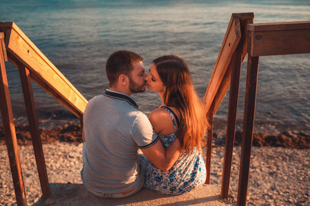 Portrait of a couple of lovers embrace sitting on the stairs and pose against the background of the sea. Back view. The concept of Valentine's day.の写真素材