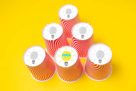 Paper cups arranged in a pyramid with a picture of a light bulb on the bottom. Yellow background....