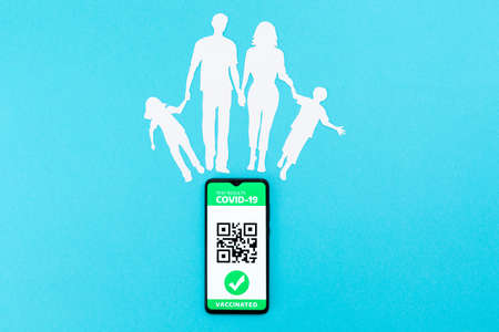 Cellphone with app of digital immunity passport and a silhouette of a family cut out of paper on a...